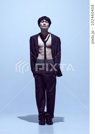 Portrait of young stylish man posing in black jacket on naked body with tie and classical pants against light blue studio background 102460408