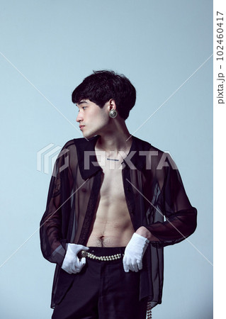Portrait of handsome young guy wearing elegant, transparent, black shirt on naked body, posing against light blue studio background 102460417