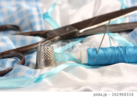 Spool of Blue Thread, Thimble and Needle on Blue and White Fabric Spool of Blue Thread, Thimble and Needle on Blue and White Fabric 102468318
