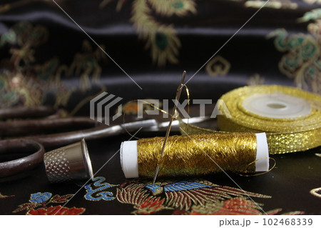Spool of Gold Thread With Thimble on Vintage Black Silk Fabric Spool of Gold Thread With Thimble on Vintage Black Silk Fabric 102468339