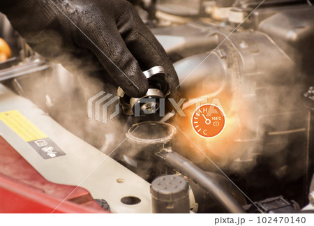 Auto mechanic hand opens the radiator cap with steam escaping around the engine compartment. 102470140
