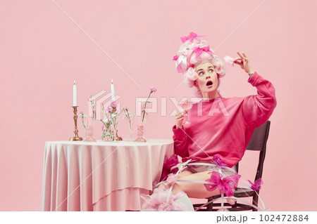 Portrait gorgeous queen wearing big pink wig holding wine glass with exciting face over pink studio background. Sweet cocktails 102472884