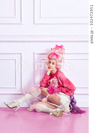 Portrait of young girl, sad princess wearing elegant pink clothes, and peruke holding candies over luxury interior background Portrait of young girl, sad princess wearing elegant pink clothes, and peruke holding candies over luxury interior background 102472951