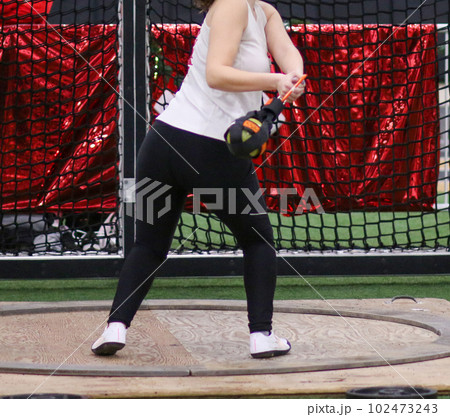 Female high school track athlete in the circle throwing a wieght during a weight throw competition 102473243