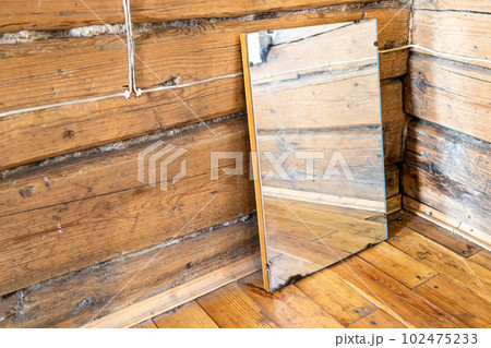 old mirror stands on wooden flooring in log house 102475233