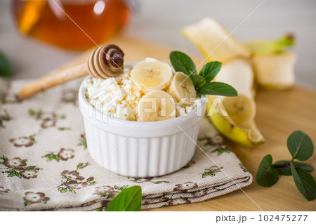 crumbly organic cottage cheese with honey and bananas in a ceramic bowl 102475277