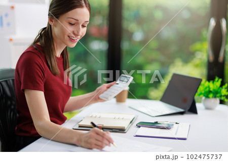 Concept of business office woman working,Businesswoman smile while working about her invesment plan with analyzing document and business investment graph data by using laptop on desk in workstation. 102475737