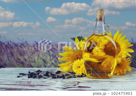 A bottle of oil, fresh sunflower flowers and seeds on the table, against the backdrop of a landscape with a flowering field, organic products, harvest, farm, sale, agriculture A bottle of oil, fresh sunflower flowers and seeds on the table, against the backdrop of a landscape with a flowering field, organic products, harvest, farm, sale, agriculture 102475901