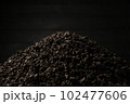 A pile of black fanning or broken loose leaf tea on a dark black background. Close-up, side view. 102477606