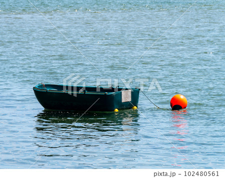 A small single-person plastic boat on the surface of the water. Orange buoy on the water near the boat.  boat on body of water 102480561