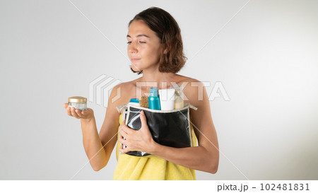 A woman with a cosmetic bag and face cream in her hands after a shower - a procedure for self-care at home 102481831