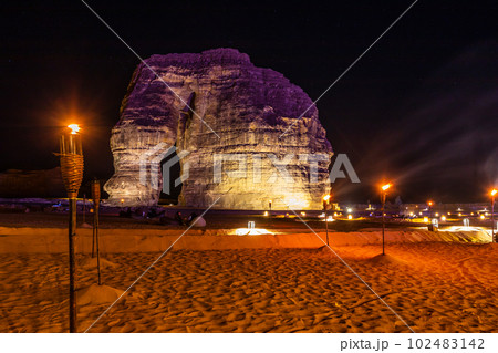 Illuminated by burning torches sandstone elephant rock erosion monolith standing in the night desert, Al Ula, Saudi Arabia 102483142