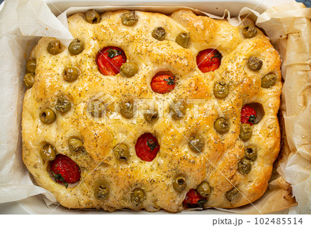 Overhead of Traditional Italian Homemade Flat Bread Focaccia with Green Olives, Olive Oil, Cherry Tomatoes and Rosemary in Baking Tray on Rustic Dark Blue Stone Background Overhead of Traditional Italian Homemade Flat Bread Focaccia with Green Olives, Olive Oil, Cherry Tomatoes and Rosemary in Baking Tray on Rustic Dark Blue Stone Background 102485514