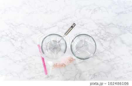 Flat lay. Sifting crushed peppermint candies through the spider strainer into the glass mixing bowls. 102486106