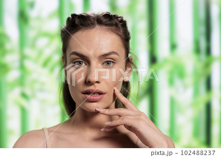 Young caucasian skincare model posing with fingers on face portrait. Natural beautiful woman showing glowing skin after organic cosmetology treatment on bamboo background 102488237