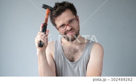 Young caucasian worker man holding a hammer isolated on grey background 102489262