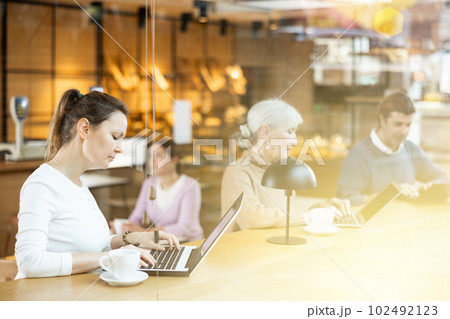 Smiling woman using laptop and drinking coffee in modern cafe 102492123