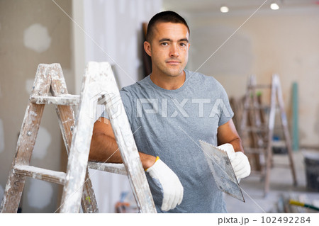 Portrait of a young man standing with a construction trowel in his hands Portrait of a young man standing with a construction trowel in his hands 102492284