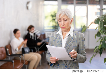 Upset aged female employee standing in office with papers 102492469