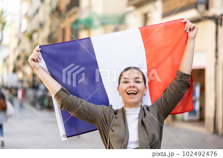 Patriotic young woman waving the flag of France on city street 102492476