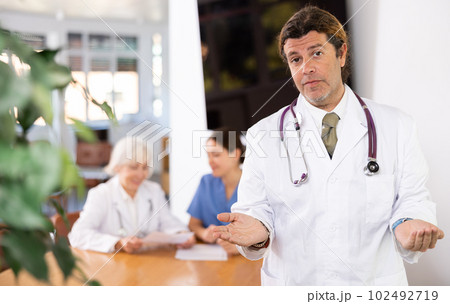Professional doctor politely inviting patients in medical office 102492719
