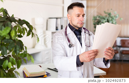 Male doctor reading documents at clinic Male doctor reading documents at clinic 102492873