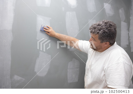 Contractor sanding wall after putty has been applied during repair improvement renovation of an apartment 102500413