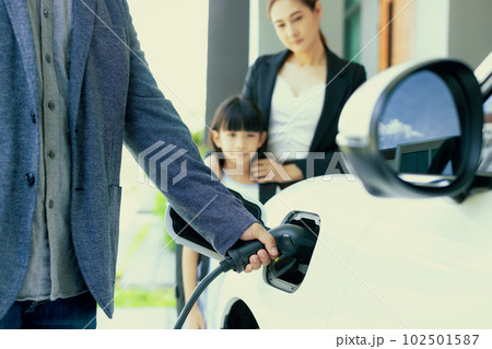 Focus hand charging progressive EV car with blurred family background. Focus hand charging progressive EV car with blurred family background. 102501587