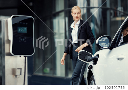 Focus EV charging station for electric car with blur progressive businesswoman. Focus EV charging station for electric car with blur progressive businesswoman. 102501736