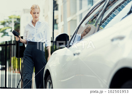 Progressive businesswoman plugs charger plug from charging station to EV. 102501953