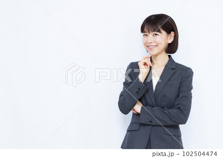 白い背景の前で笑顔で考えているスーツ姿の30代女性 白い背景の前で笑顔で考えているスーツ姿の30代女性 102504474