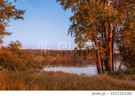Landscape with a river and a forest in the rays of the setting sun. The end of summer. August. The beginning of autumn. Copy space 102510188
