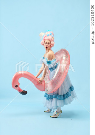Portrait with funny beautiful princess, queen wearing dress holding pink inflatable flamingo and going beach over blue background Portrait with funny beautiful princess, queen wearing dress holding pink inflatable flamingo and going beach over blue background 102510400