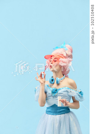 Portrait with princess, queen wearing dress playing with soap bubbles and smiling over blue studio background. Vivid emotions 102510408