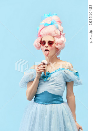 Young princess, queen wearing sunglasses eating ice cream and looking at camera over blue studio background Young princess, queen wearing sunglasses eating ice cream and looking at camera over blue studio background 102510482