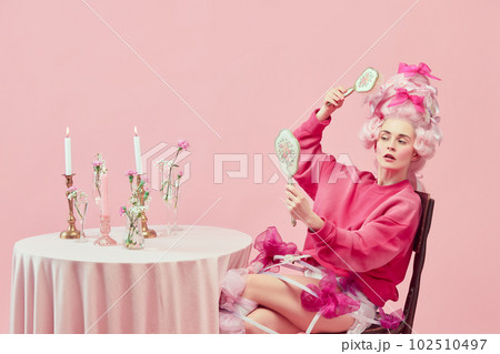 Portrait with princess wearing fancy pink clothes holding hand mirror and doing hairstyle over pink background. Beauty salon Portrait with princess wearing fancy pink clothes holding hand mirror and doing hairstyle over pink background. Beauty salon 102510497