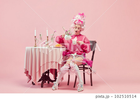 Portrait of elegant princess, queen wearing pink clothes, and wig drinking tea over pink background. Pink style festive table Portrait of elegant princess, queen wearing pink clothes, and wig drinking tea over pink background. Pink style festive table 102510514