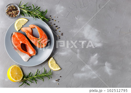 Steak of fresh raw red fish salmon with lemon, rosemary and pepper on grey background Steak of fresh raw red fish salmon with lemon, rosemary and pepper on grey background 102512795