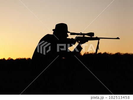 Hunting, sunset, man with gun and focus on target in nature to hunt game for sport on safari adventure. Sky, silhouette and hunter with rifle in bush, setting sun and shooting hobby on summer evening 102513458