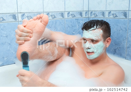 Man with mask on his face is peeling his foot sitting in bathroom at home. 102514742