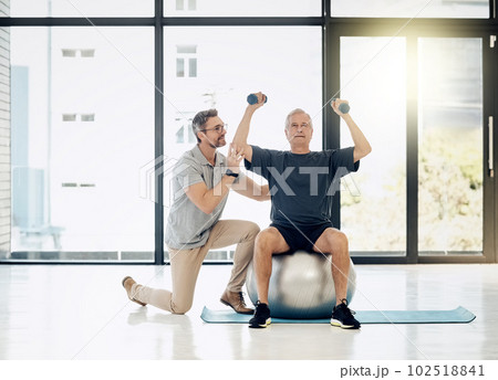 Hes getting a little stronger with every session. a friendly physiotherapist helping his mature patient to use dumbbells in a rehabilitation center. 102518841
