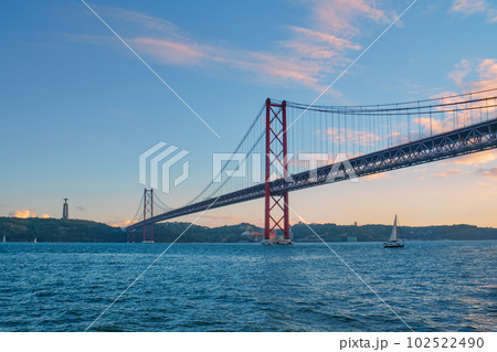 View of 25 de Abril Bridge famous tourist landmark of Lisbon connecting Lisboa to Almada on Setubal Peninsula over Tagus river with tourist yacht boats passing under. Lisbon, Portugal 102522490
