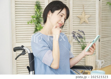 リビングでスマートフォン使う車椅子に乗った女性 102523323