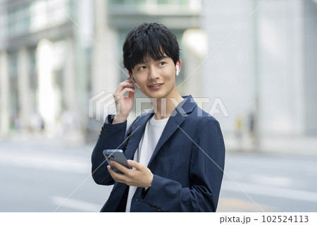 スマートフォンを持ってイヤホンをつけた20代の男性 スマートフォンを持ってイヤホンをつけた20代の男性 102524113