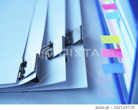 テーブルに置かれた青いファイルとクリップで綴じた書類 102524710