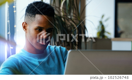 Close up of concentrated young african man in headphones with laptop computer working at home office. Remote job, technology and people concept 102526748