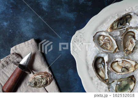Plate with fresh opened oysters and oyster opener on a blue background, top view Plate with fresh opened oysters and oyster opener on a blue background, top view 102532018