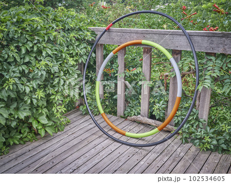 weighted hula hoop and one home made from a sprinkler pipe on a wooden backyard deck in summer scenery, core workout concept 102534605