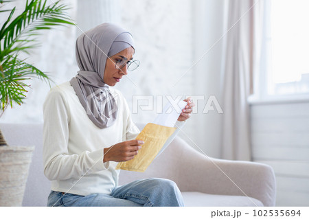 Upset young Arab female student in hijab looking at camera and holding letter in envelope she received home delivery. Notification of rejection, exam results. Upset young Arab female student in hijab looking at camera and holding letter in envelope she received home delivery. Notification of rejection, exam results. 102535694
