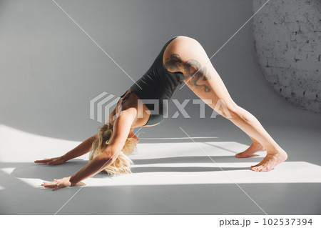 a sexy blonde with tattoos in a leather swimsuit performs sports exercises  102537394